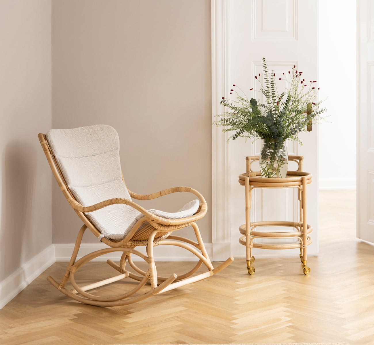 Esta es una imagen de estilo de vida de Monet Rocking Chair i natural rattan. En una habitación con paredes rosa, parqué en espiga y eucalipto.