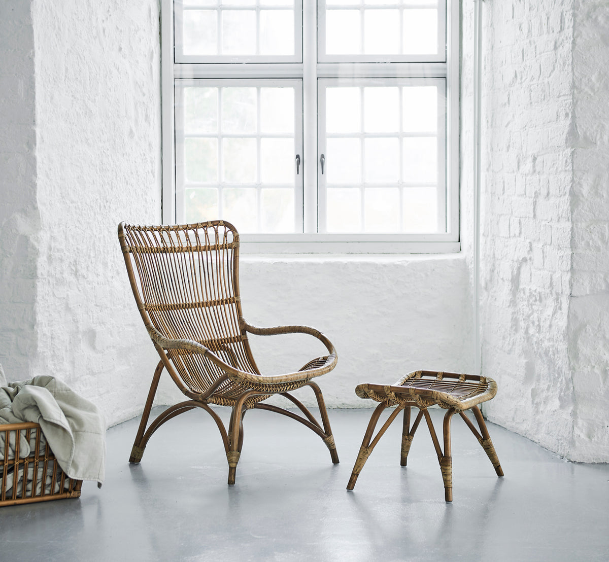 Esta es una imagen de estilo de vida de Monet Lounge Chair i antique rattan. En una habitación con papel tapiz de mariposas y faroles marroquíes decorativos.