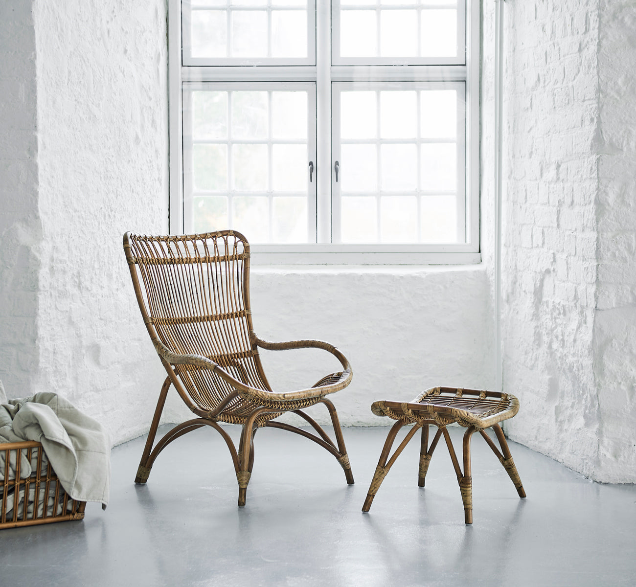 Esta es una imagen de estilo de vida de Monet Lounge Chair i antique rattan. En una habitación con papel tapiz de mariposas y faroles marroquíes decorativos.
