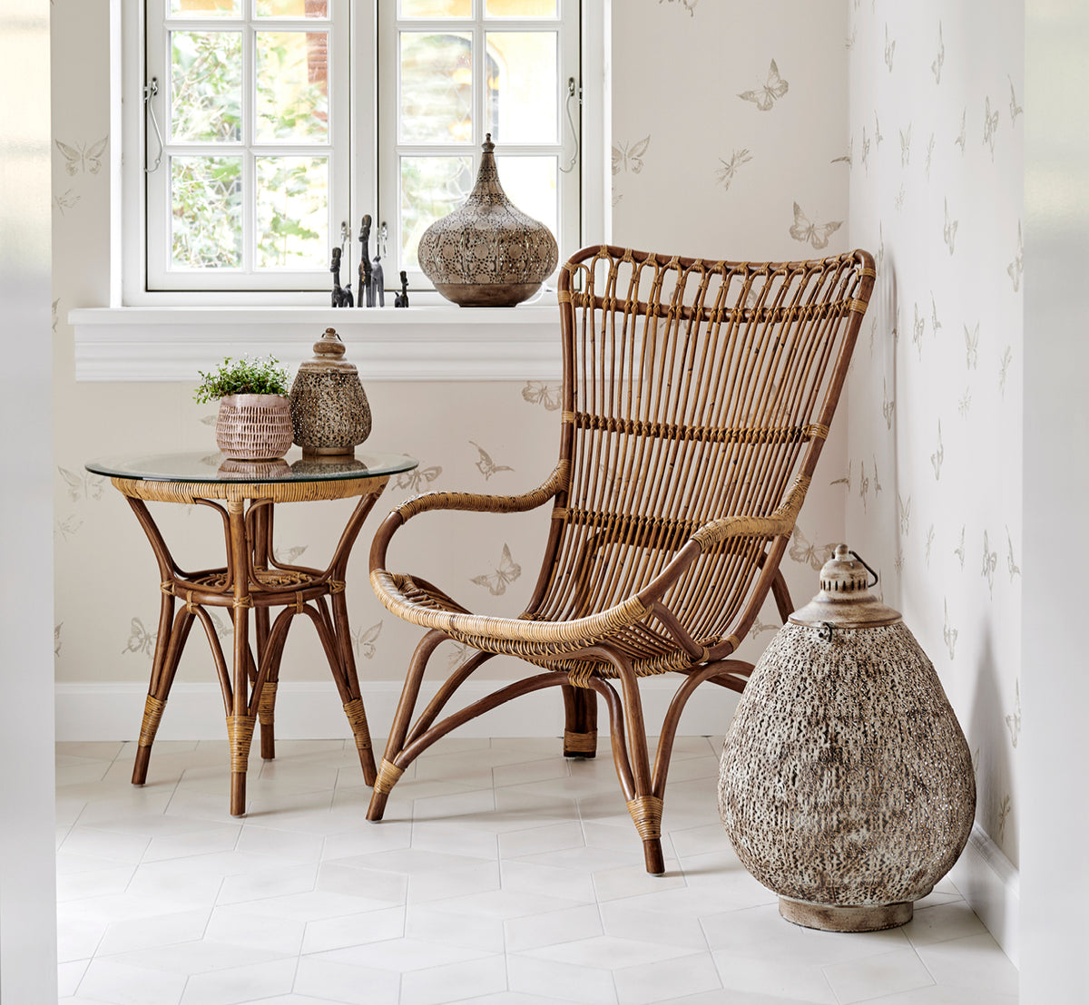 Esta es una imagen de estilo de vida de Monet Lounge Chair i antique rattan. Con reposapiés en una sala rústica blanca con textil azul marino oscuro.