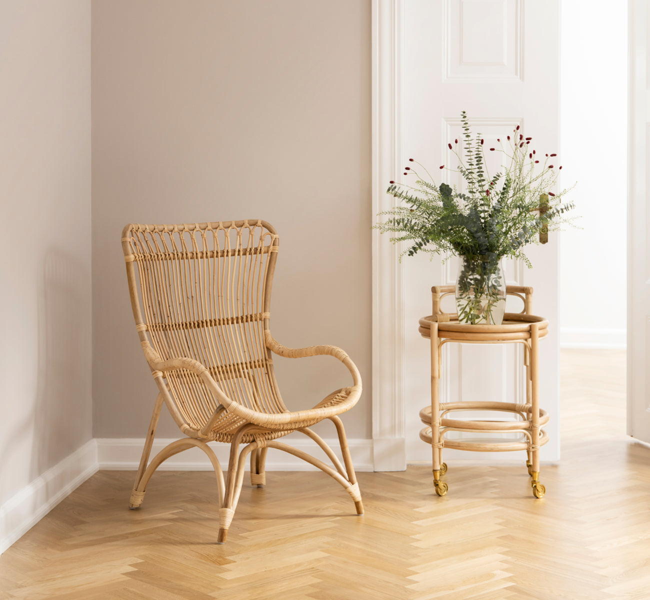 Esta es una imagen de estilo de vida de Monet Lounge Chair i natural rattan. Con reposapiés y mesa auxiliar en un granero rústico oscuro con vela.