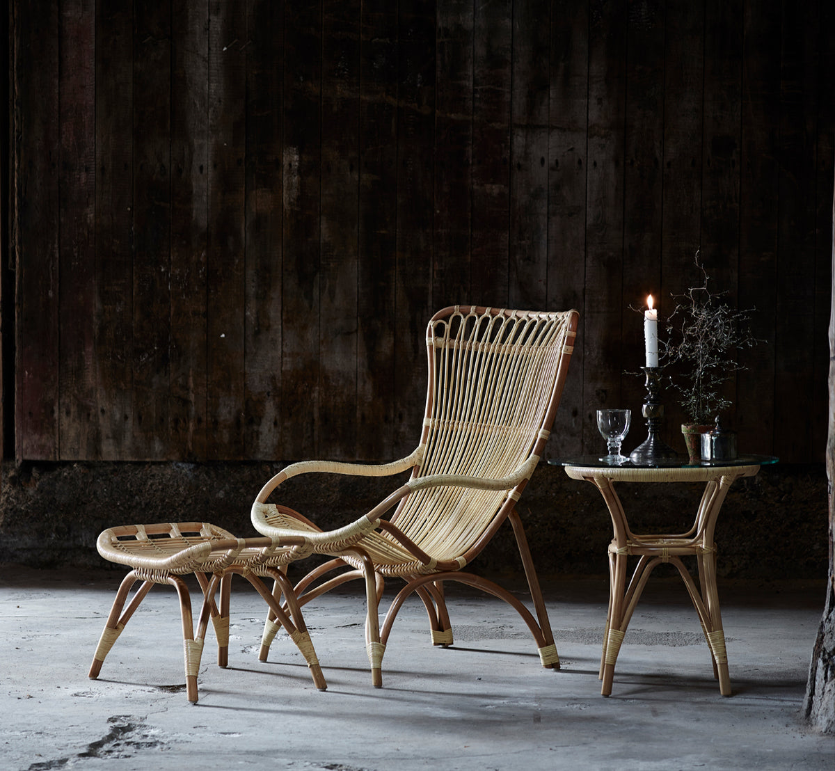 Esta es una imagen de estilo de vida de Monet sillón lounge en natural rattan. Combinada con reposapiés y mesa auxiliar contra una pared revestida de madera oscura.