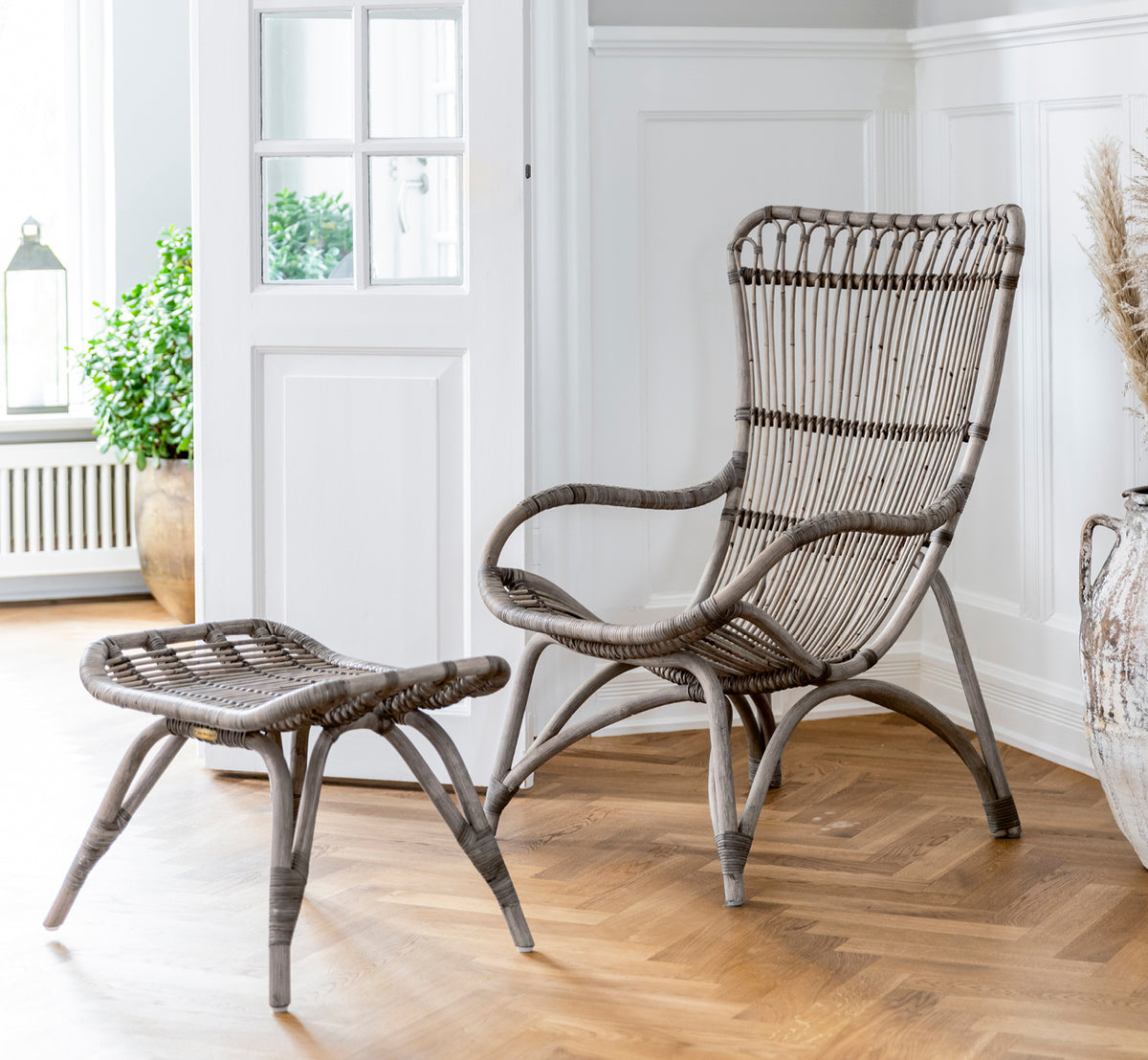 Esta es una imagen de estilo de vida de Monet Footstool i taupe rattan. Combinado con sillón lounge en un ambiente de granero oscuro con vela y cristal.