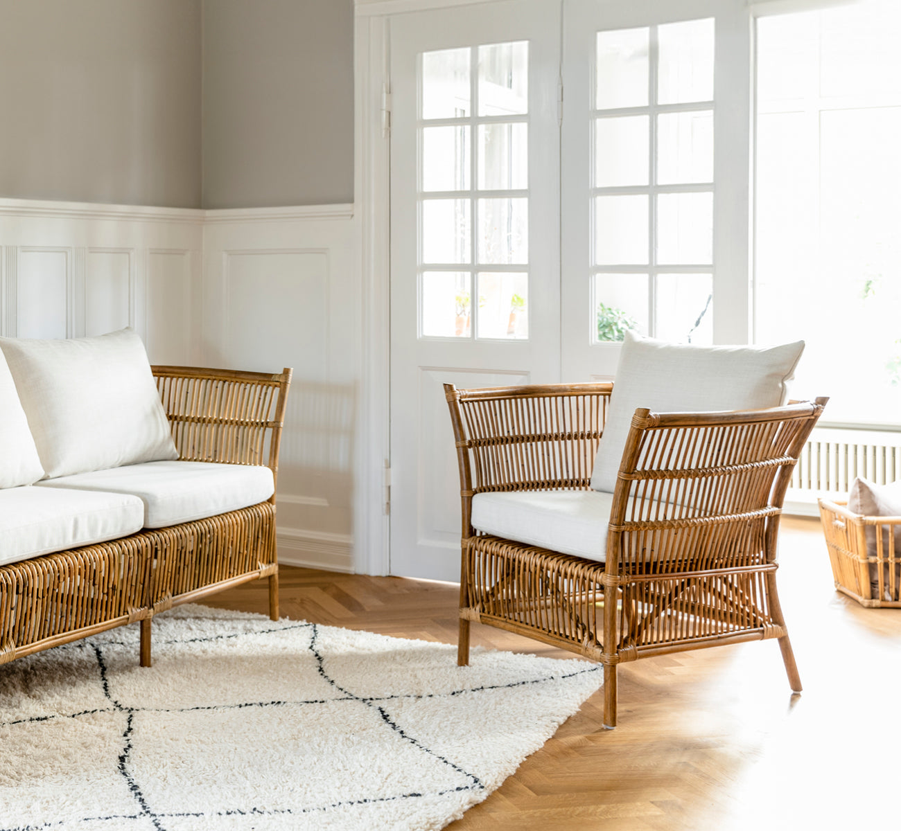 Esta es una imagen de estilo de vida de Donatello sillón lounge en antique rattan, en una luminosa sala de estar con parqué en espiga y exuberante.