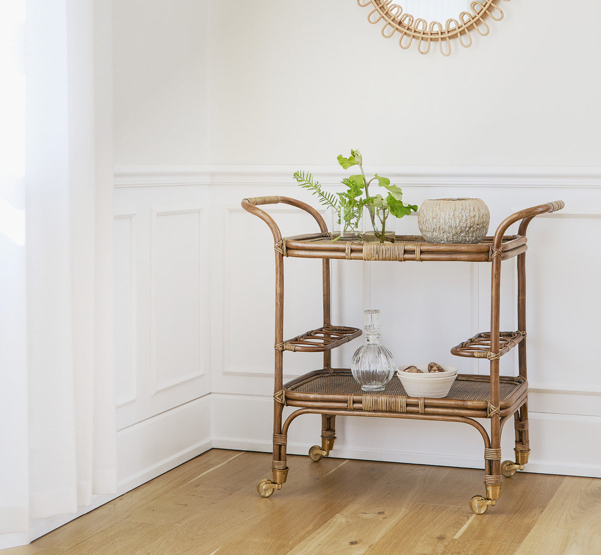 Esta es una imagen de estilo de vida de Carlo Trolley en antique Rattan, en un interior blanco y luminoso con revestimiento de pared y espejo de.