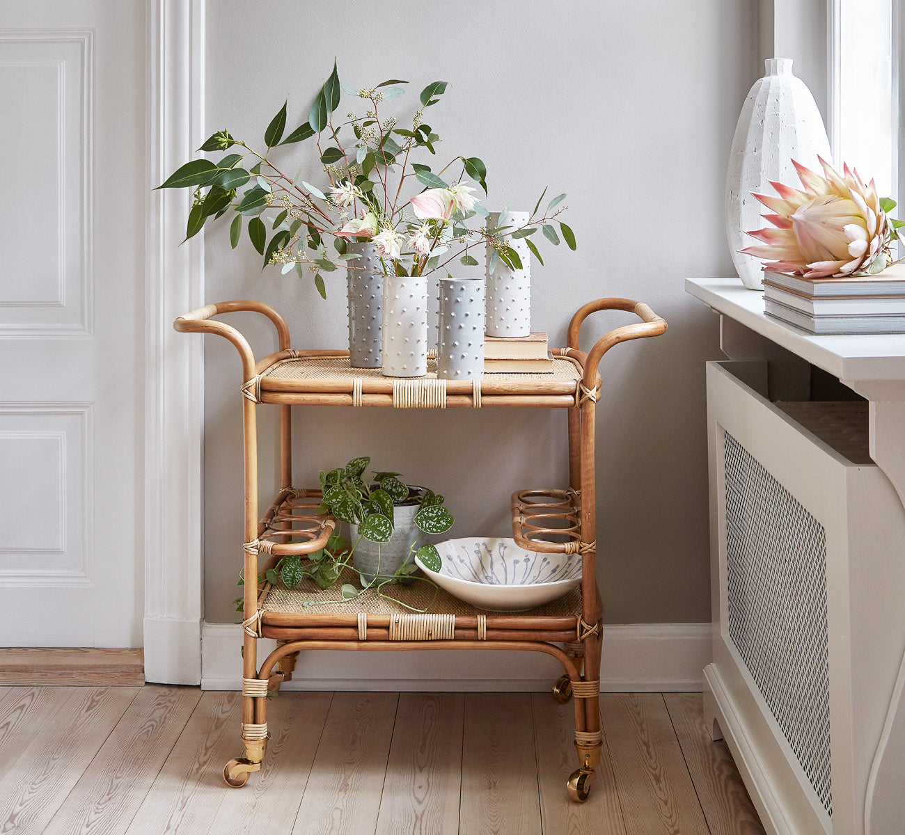 Esta es una imagen de estilo de vida de Carlo Trolley en antique Rattan, en un interior blanco y luminoso con revestimiento de pared y espejo de.