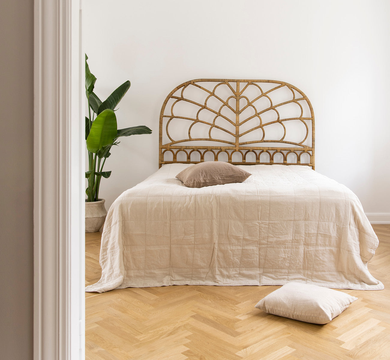 Esta es una imagen de estilo de vida de Celia cabecero en antique rattan, en un dormitorio tranquilo y luminoso con ropa de cama neutra y parqué en.