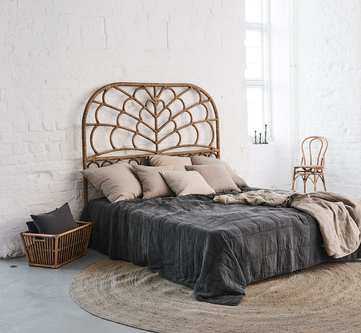 Esta es una imagen de estilo de vida de Celia cabecero en antique rattan, en un dormitorio tranquilo y luminoso con ropa de cama neutra y parqué en.
