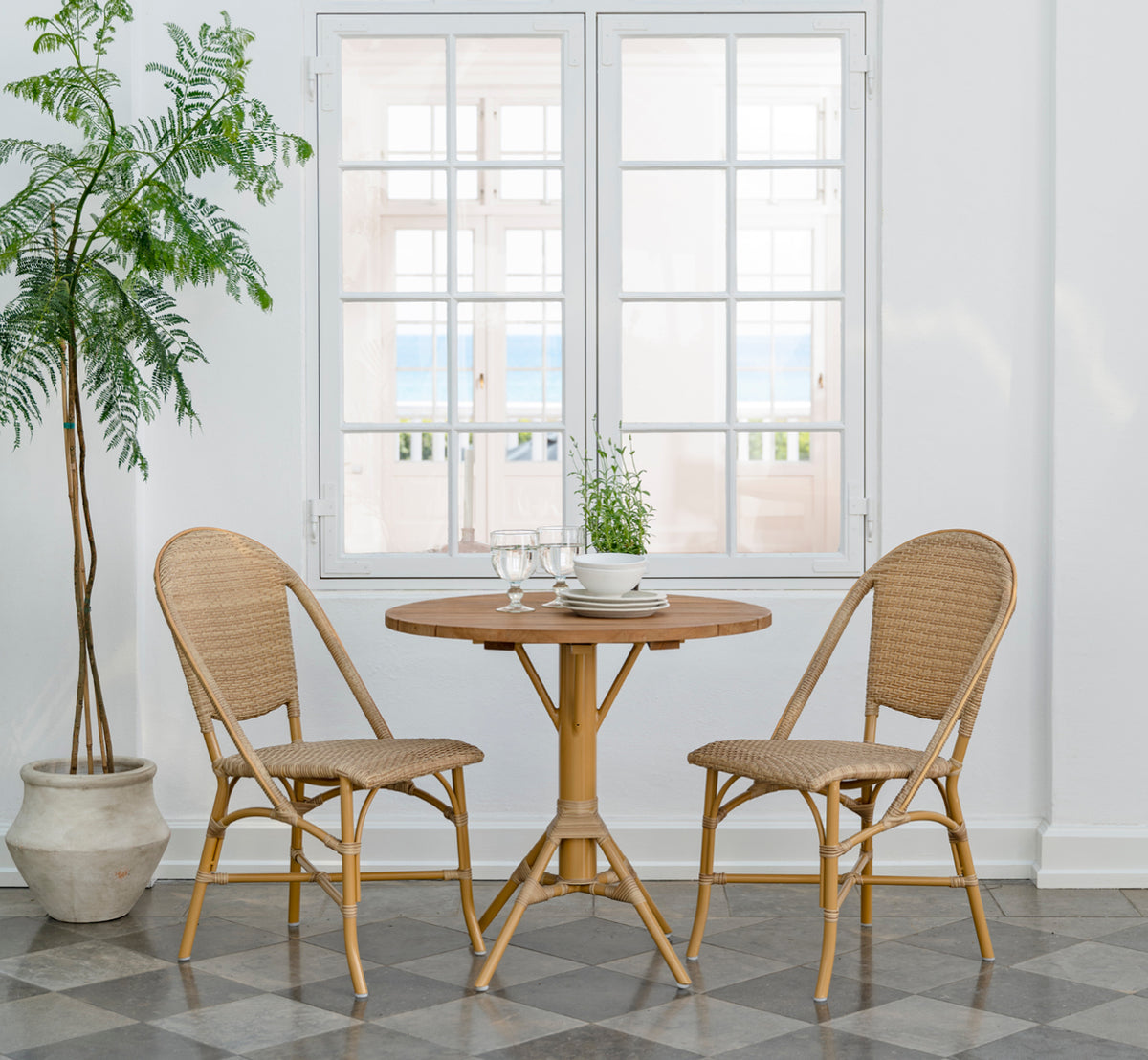 Esta es una imagen de estilo de vida de Sofie Exterior Dining Chair i almond aluminium frame natural ArtFibre. Alrededor de una mesa de teca exterior.