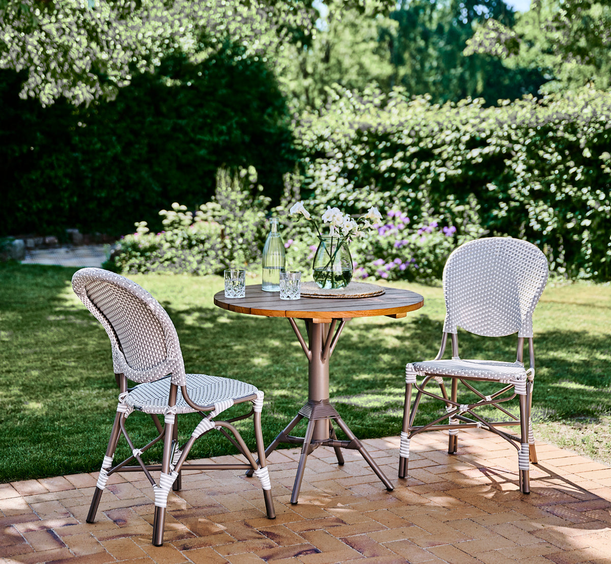 Esta es una imagen de estilo de vida de Isabell en taupe aluminium frame Grey w white dot ArtFibre, en un exuberante patio de jardín con suelo de.