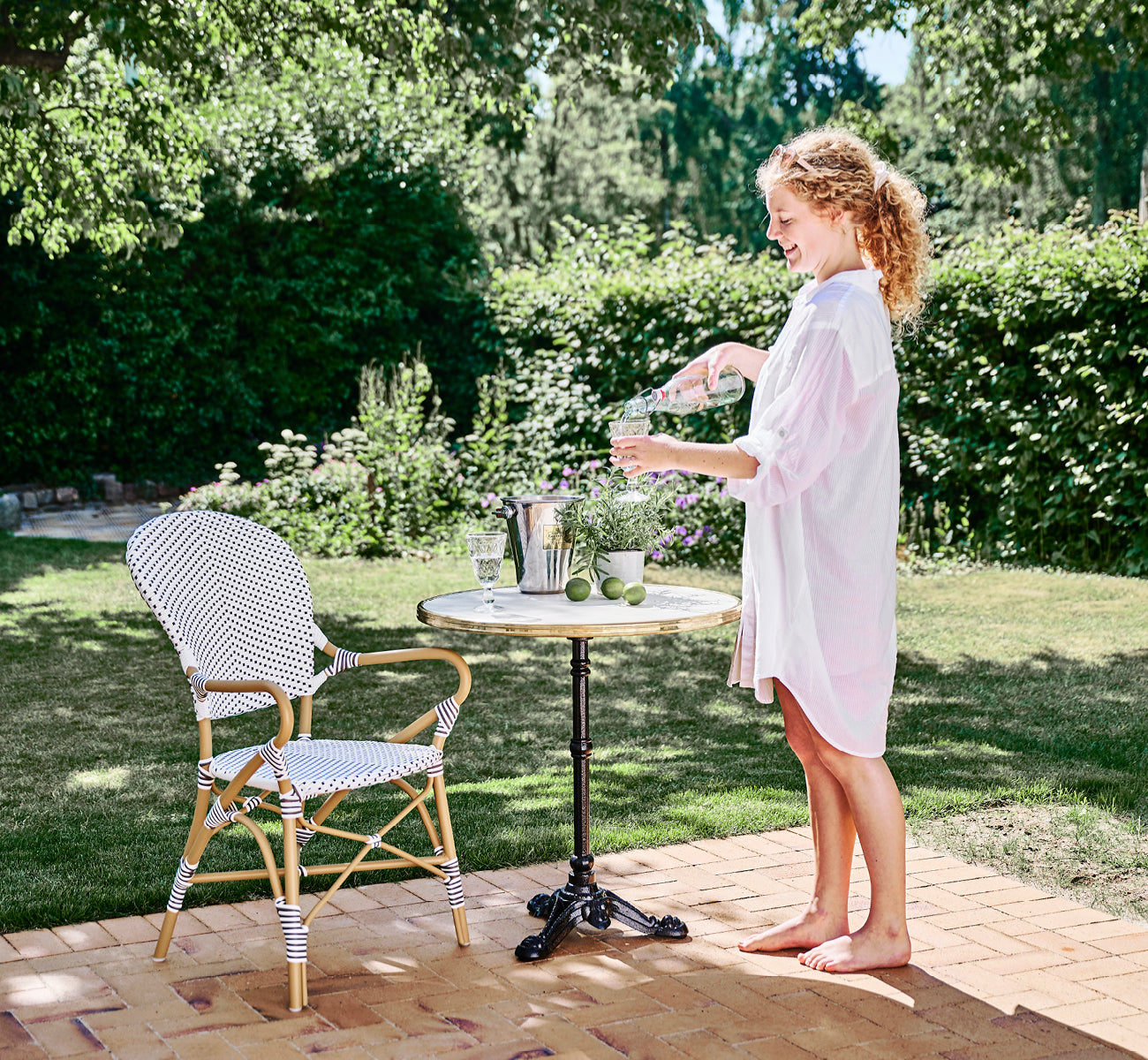 Esta es una imagen de estilo de vida de Isabell en almond aluminium frame White w cappuccino dot ArtFibre, en un exuberante patio de jardín con suelo.