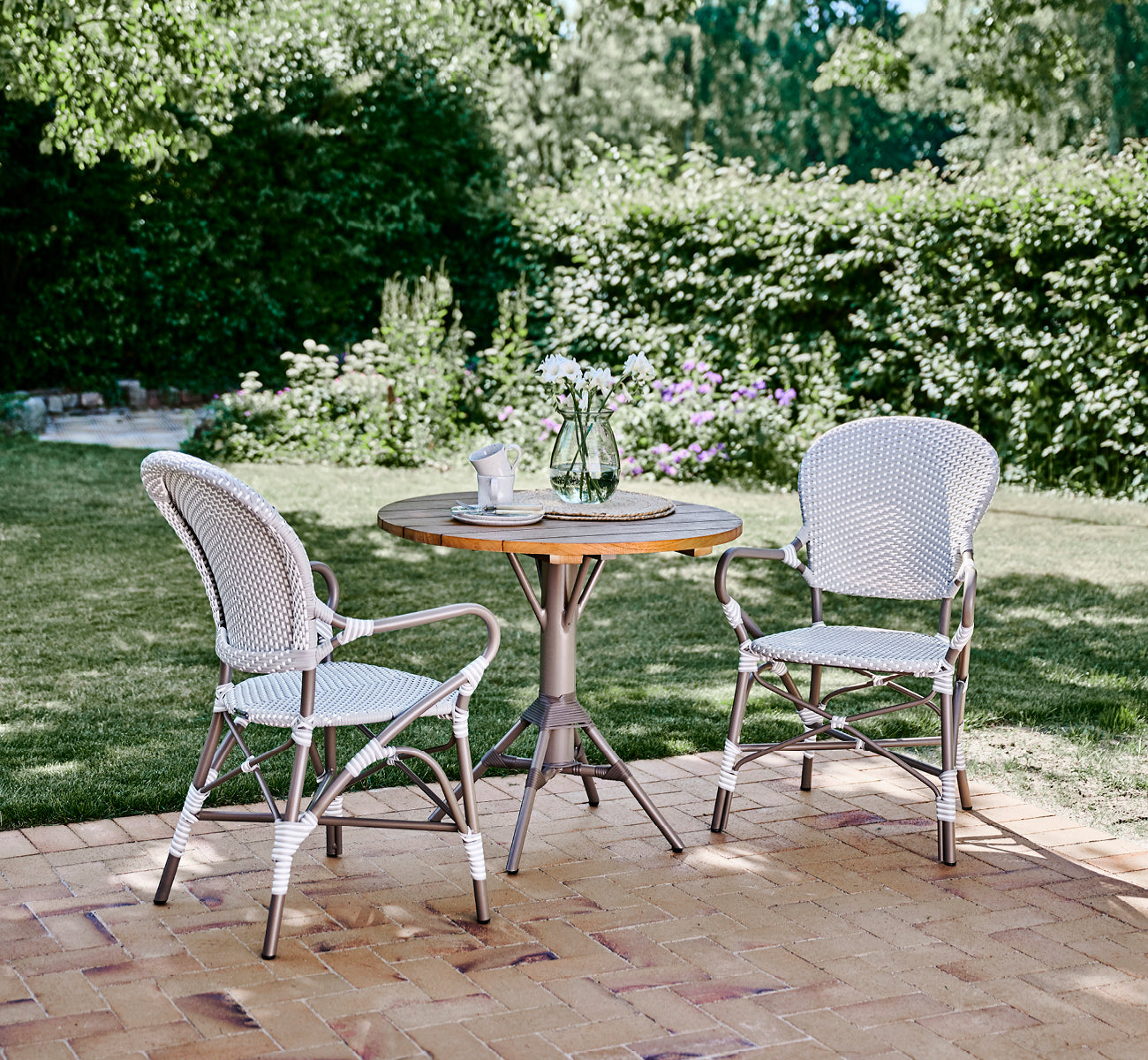 Esta es una imagen de estilo de vida de Isabell en taupe aluminium frame Grey w white dot ArtFibre, en un exuberante patio de jardín con suelo de.