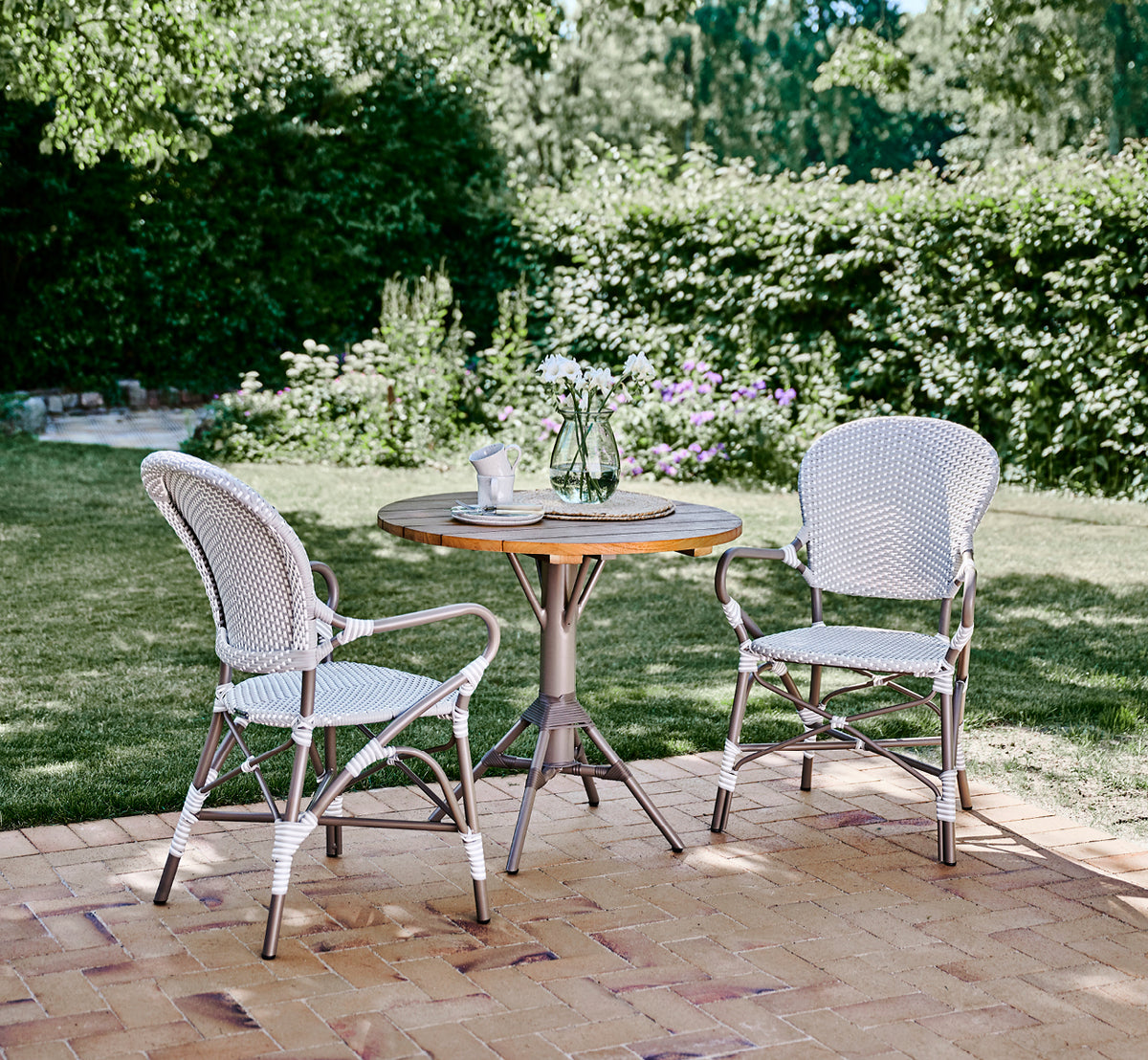 Esta es una imagen de estilo de vida de Isabell en taupe aluminium frame Grey w white dot ArtFibre, en un exuberante patio de jardín con suelo de.