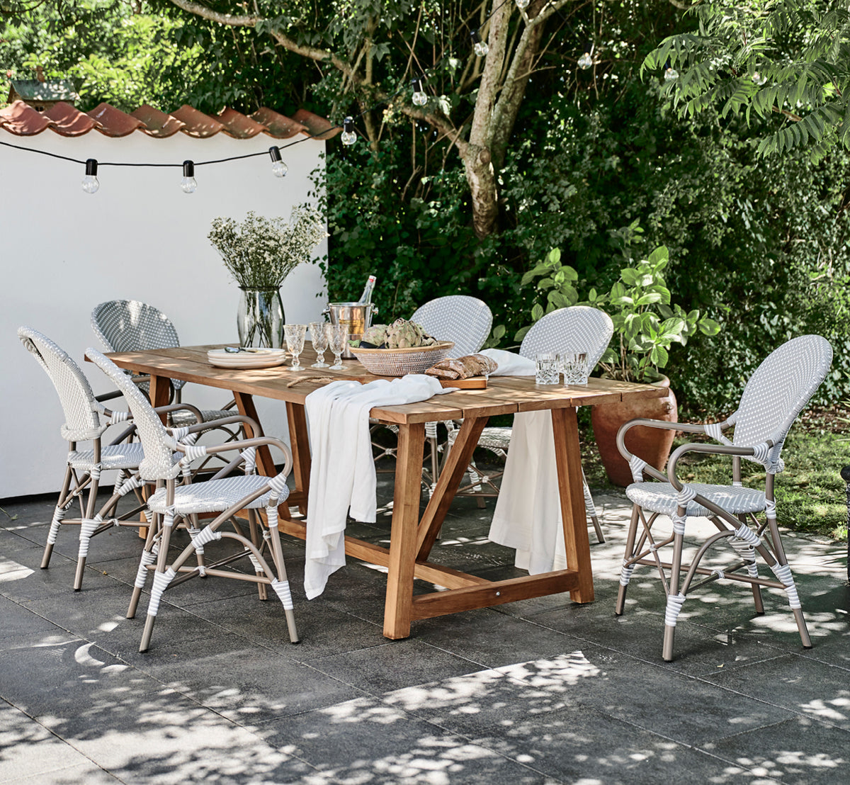 Esta es una imagen de estilo de vida de Isabell en taupe aluminium frame Grey w white dot ArtFibre, en un exuberante patio de jardín con suelo de.