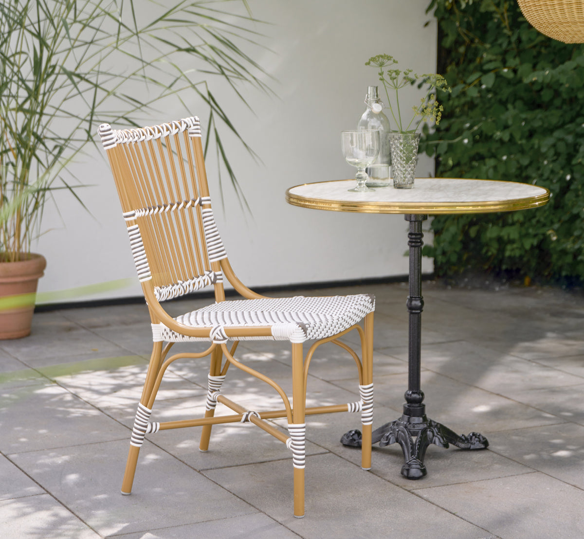 Esta es una imagen de estilo de vida de Monique Exterior Dining Chair i white w cappuccino dot ArtFibre. En una terraza soleada con palmeras.