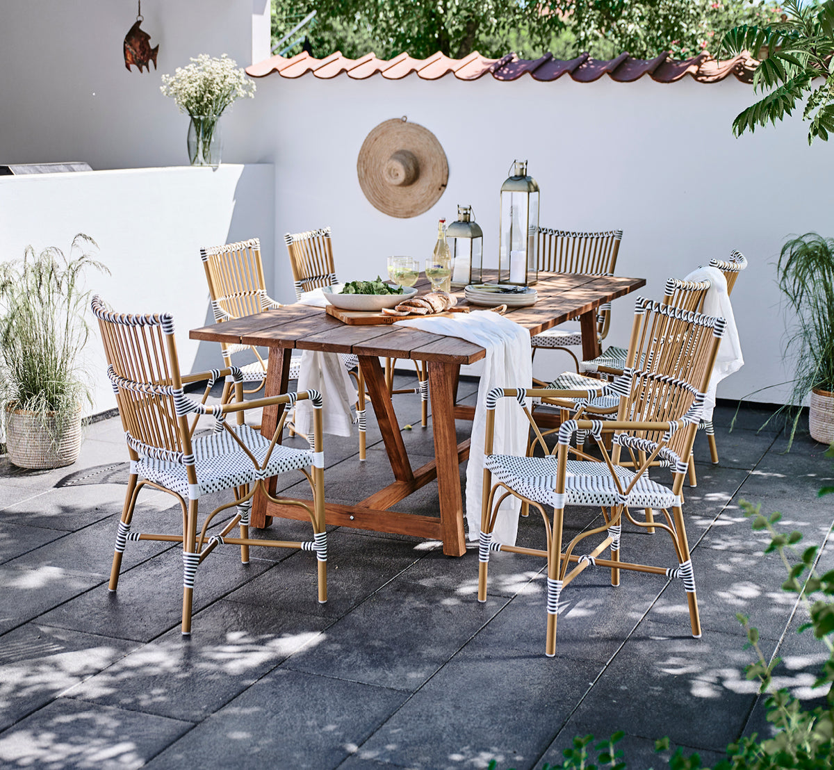 Esta es una imagen de estilo de vida de Monique Exterior Dining Armchair i white w cappuccino dot ArtFibre. Alrededor de una mesa de teca en una terraza.