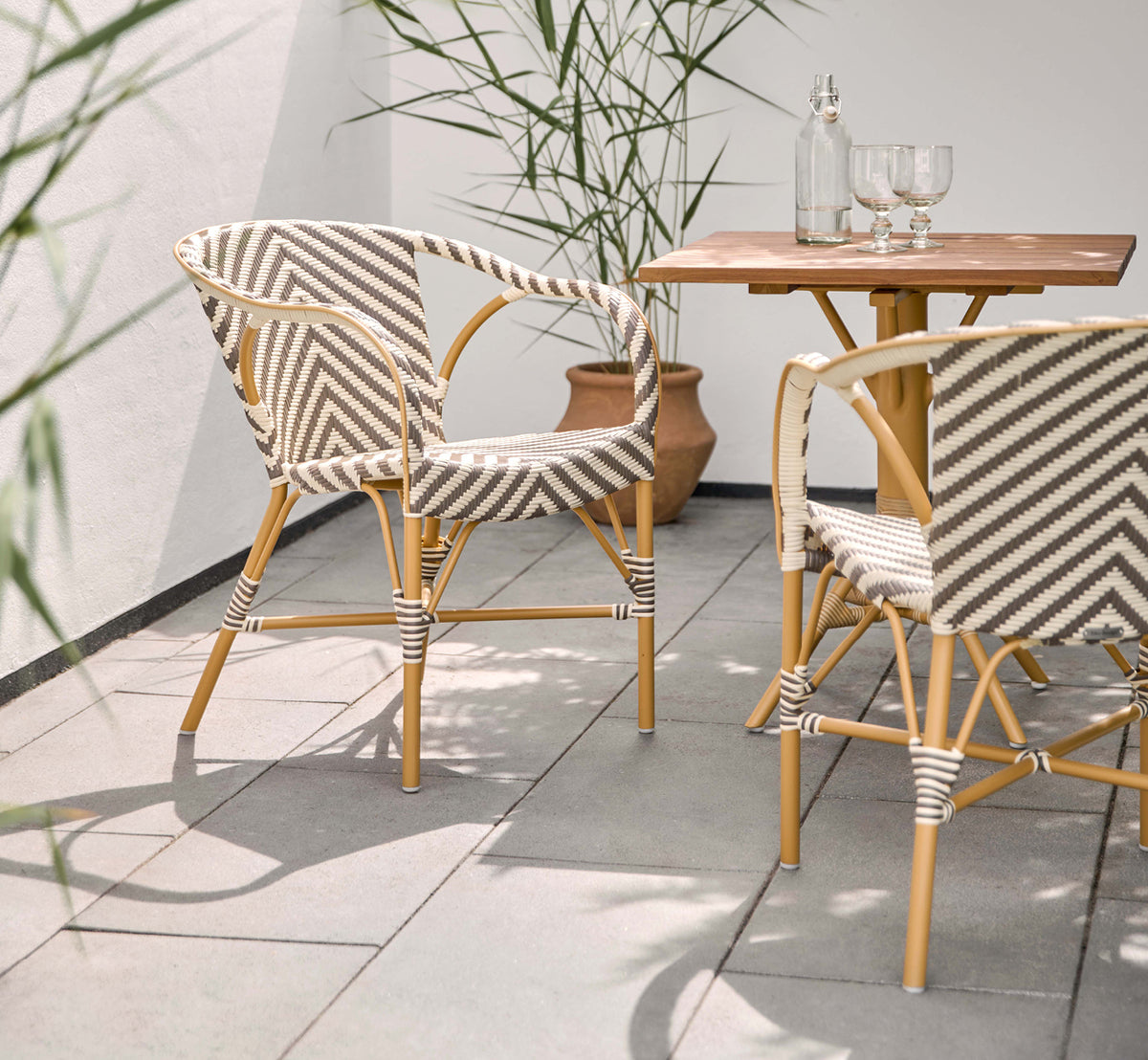 Esta es una imagen de estilo de vida de Madeleine silla de comedor exterior en almond aluminum frame chevron cappuccino ivory ArtFibre. Terraza soleada con mesa de teca.