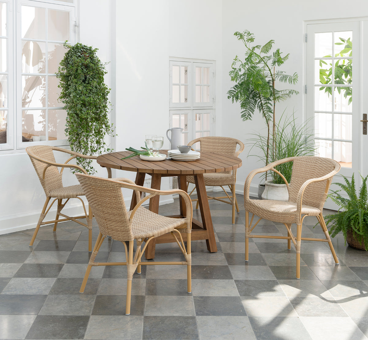 Esta es una imagen de estilo de vida de Madeleine silla de comedor exterior en almond aluminium frame natural ArtFibre. Luminoso invernadero con plantas y suelo de baldosas.