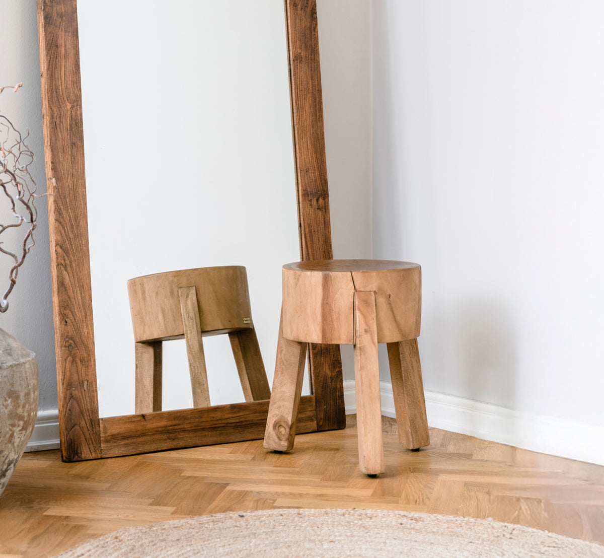 Esta es una imagen de estilo de vida de Roger taburete en teak indoor. Colocada junto a un escritorio de madera con lámpara y planta en un estudio luminoso con suelo en espiga.