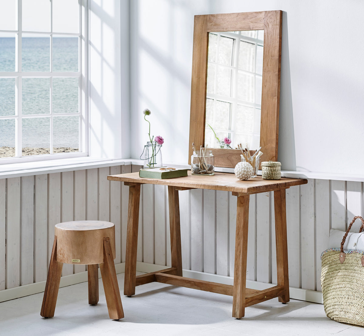 Esta es una imagen de estilo de vida de Roger taburete en teak indoor. Colocada junto a un escritorio de madera con lámpara y planta en un estudio luminoso con suelo en espiga.