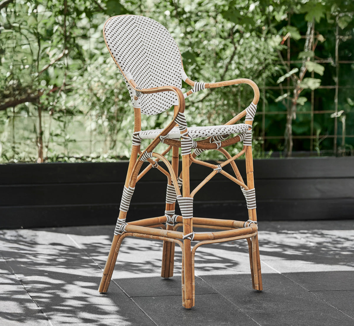 Esta es una imagen de estilo de vida de Isabell taburete de bar en white w cappuccino dot ArtFibre Skin on Rattan frame, en exterior junto a un.