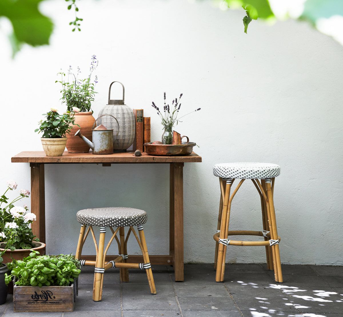 Esta es una imagen de estilo de vida de Simone taburete alto en white w cappuccino dot ArtFibre Skin on Rattan frame. Junto a una mesa con plantas.