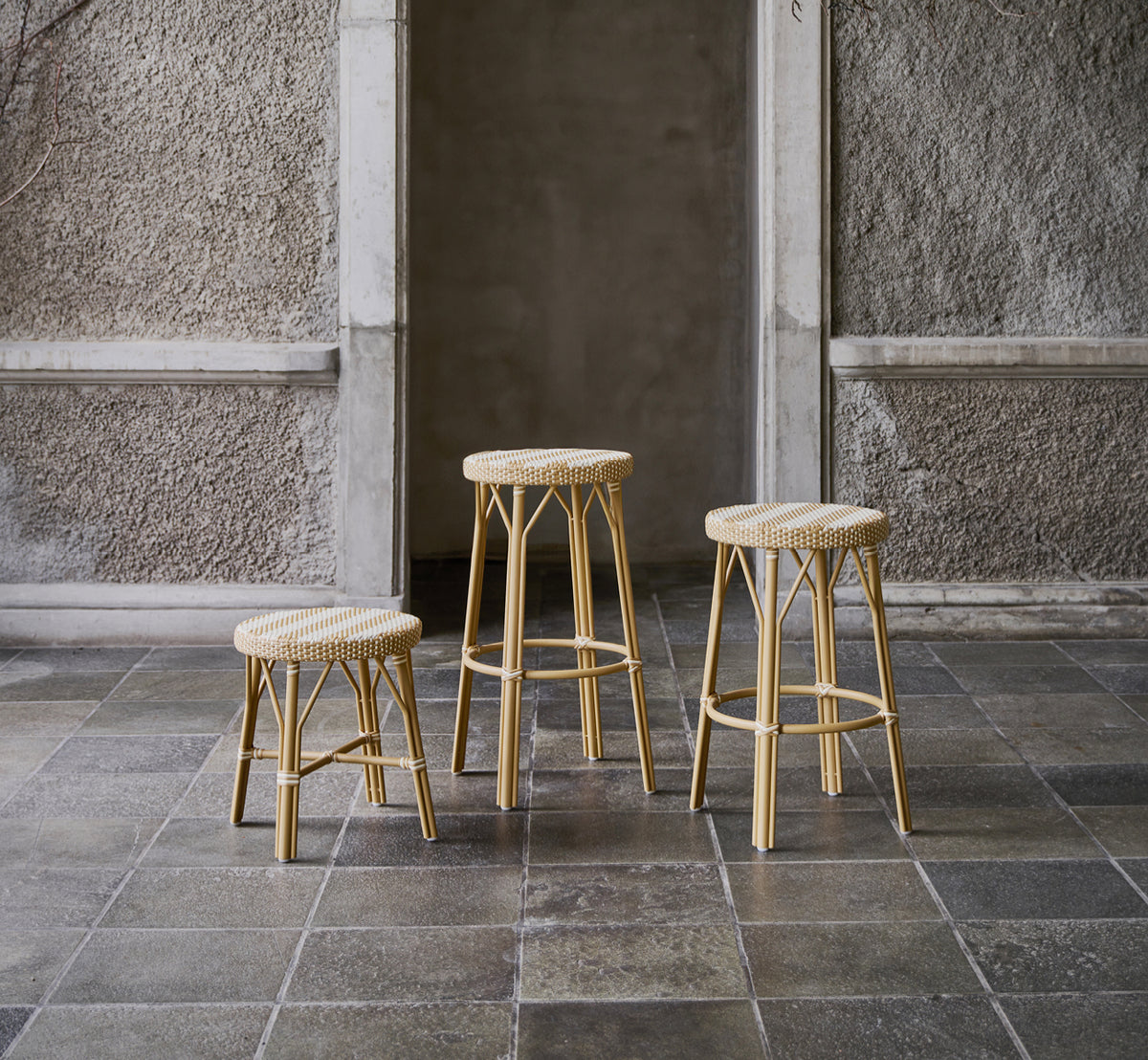 Esta es una imagen de estilo de vida de Simone taburete alto en striped honey ivory ArtFibre Skin on Rattan frame. En un patio de piedra.