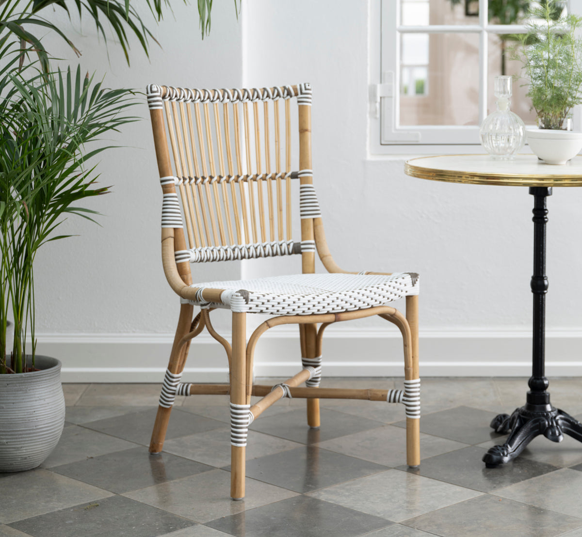 Esta es una imagen de estilo de vida de Monique silla de comedor en white w cappuccino dot artfibre skin on rattan frame. Estilizado en un interior luminoso.