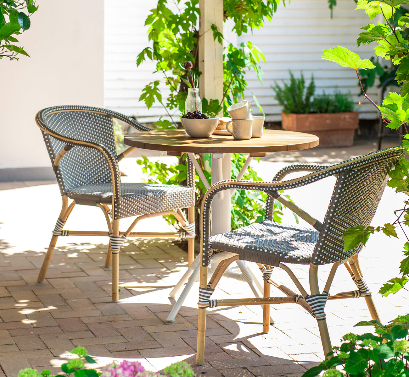 Esta es una imagen de estilo de vida de Madeleine silla de comedor en cappuccino w white dot rattan frame. Terraza sombreada con mesa redonda de teca.