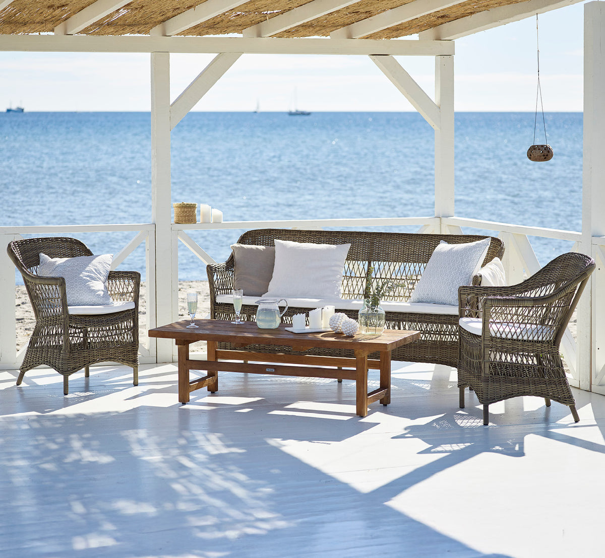 Esta es una imagen de estilo de vida de Charlot silla exterior en antique Grey ArtFibre Aluminium, en una terraza costera soleada con vistas al mar y.