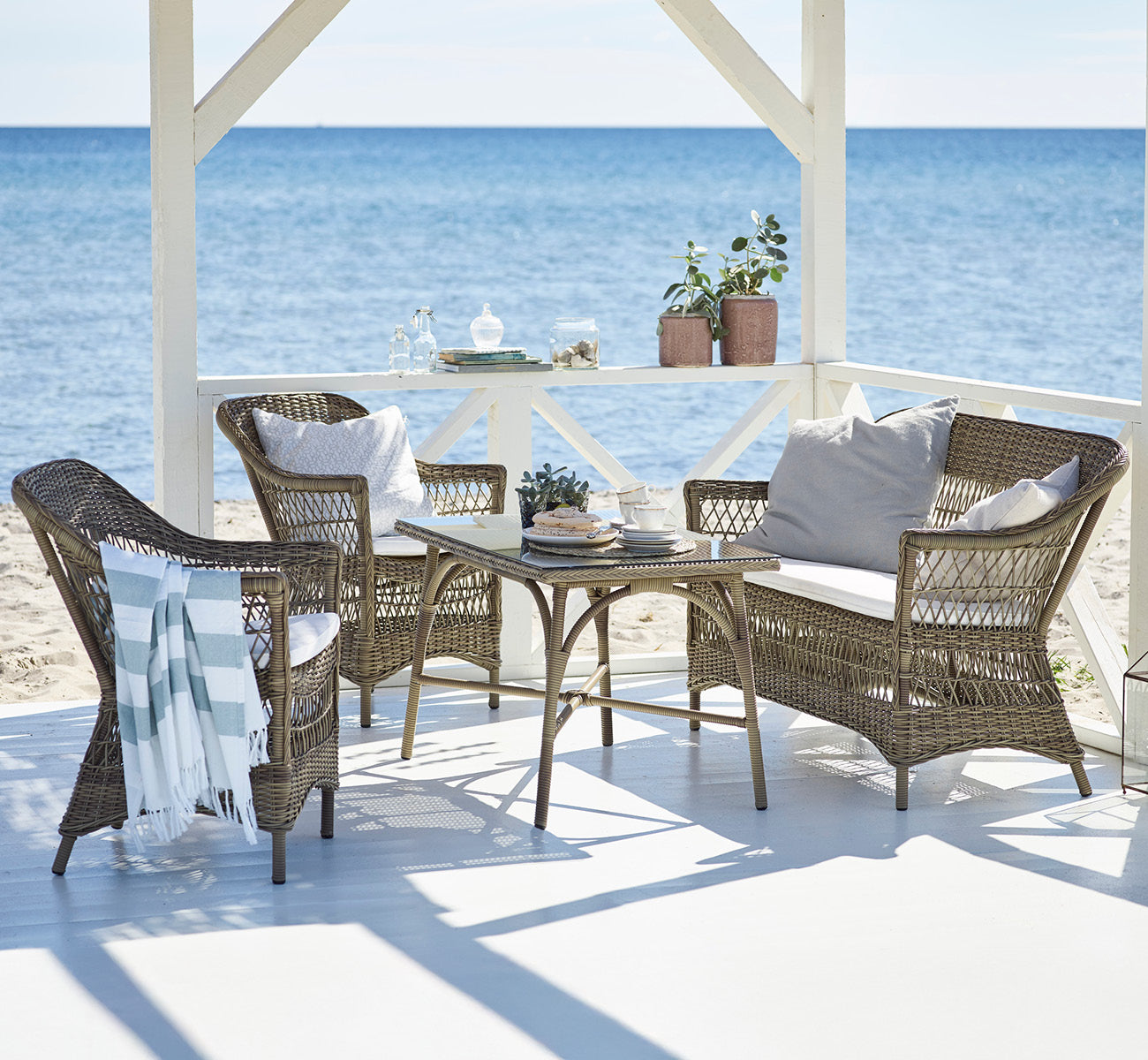Esta es una imagen de estilo de vida de Charlot silla exterior en antique Grey ArtFibre Aluminium, en una terraza costera soleada con vistas al mar y.