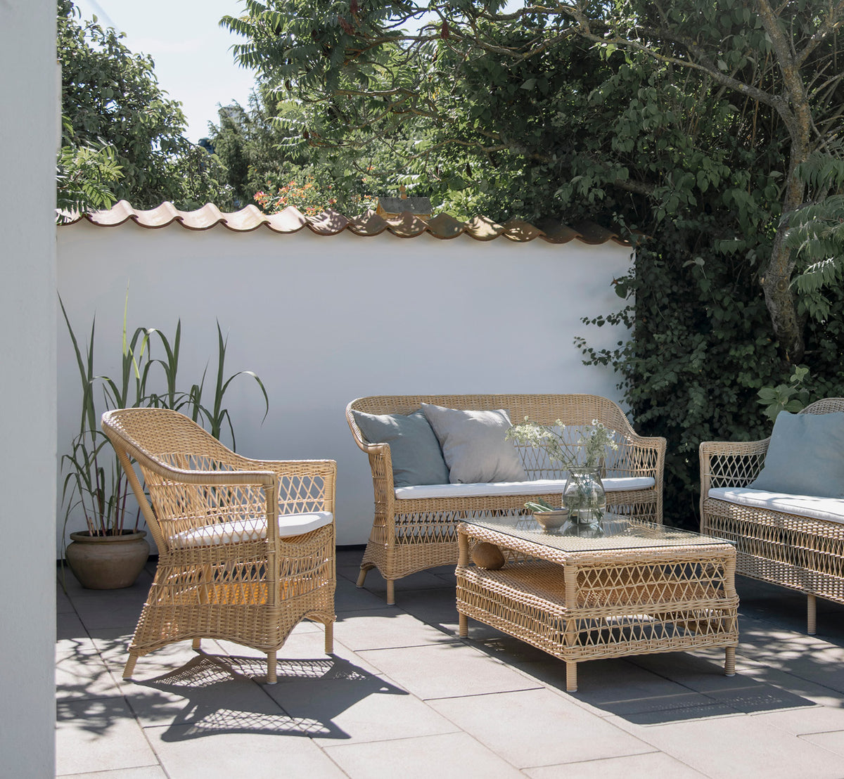 Esta es una imagen de estilo de vida de Charlot silla en natural ArtFibre Aluminium, en una terraza costera soleada con vistas al mar y una pérgola.