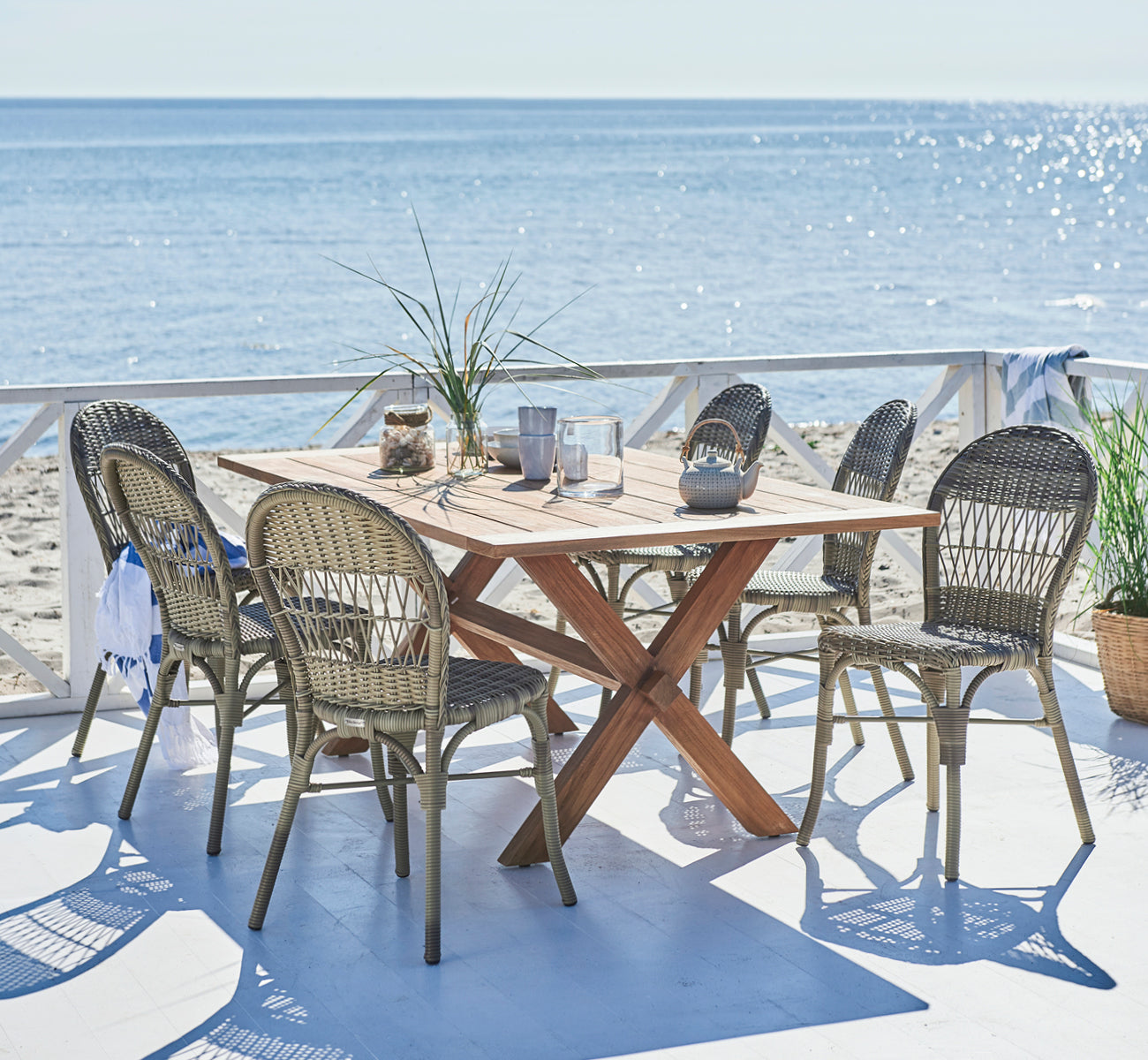 Esta es una imagen de estilo de vida de Ofelia Exterior Chair i antique grey artfibre aluminium. En una terraza de playa con vista al mar y tetera.