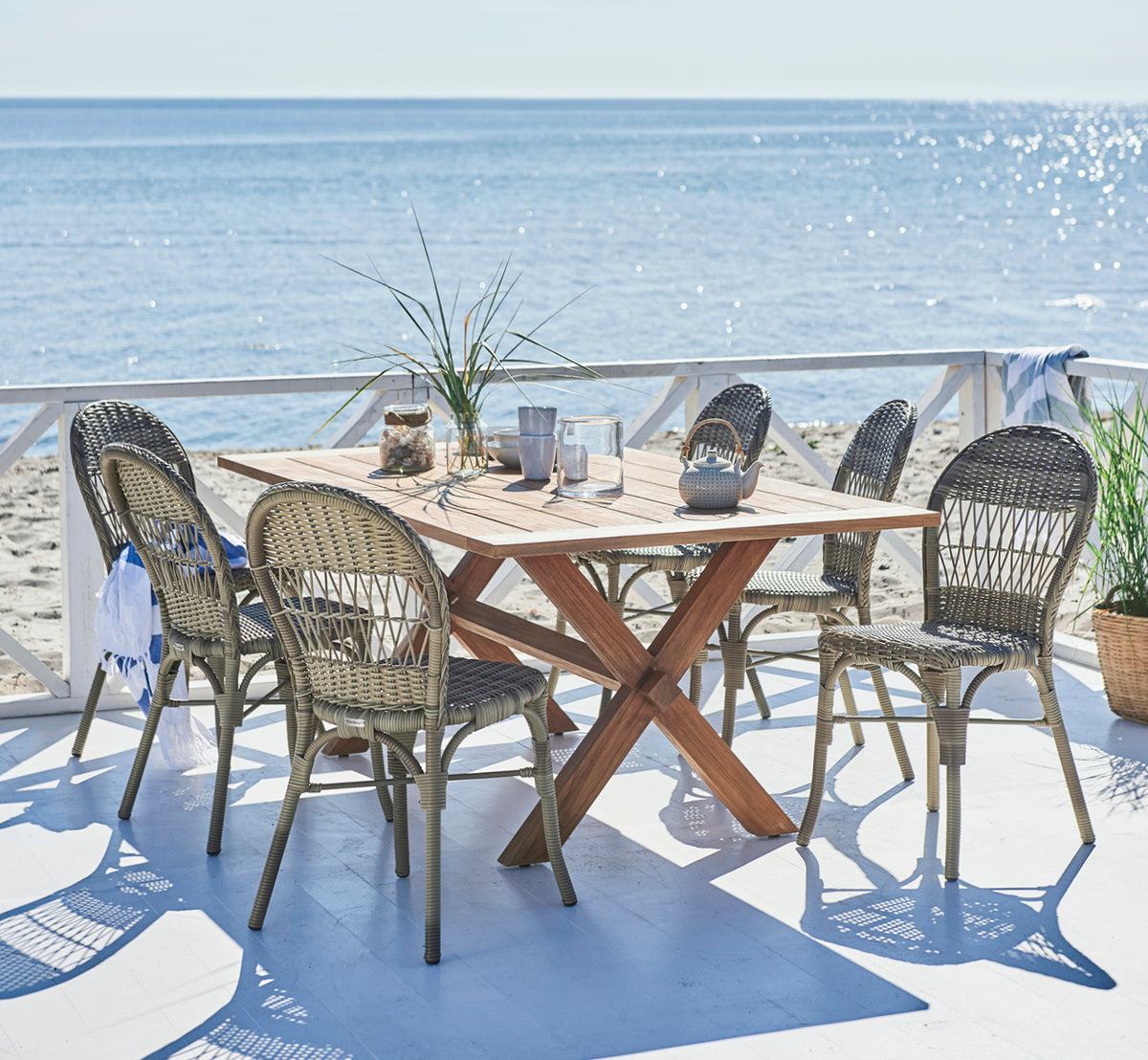 Esta es una imagen de estilo de vida de Ofelia Exterior Chair i antique grey artfibre aluminium. En una terraza de playa con vista al mar y tetera.