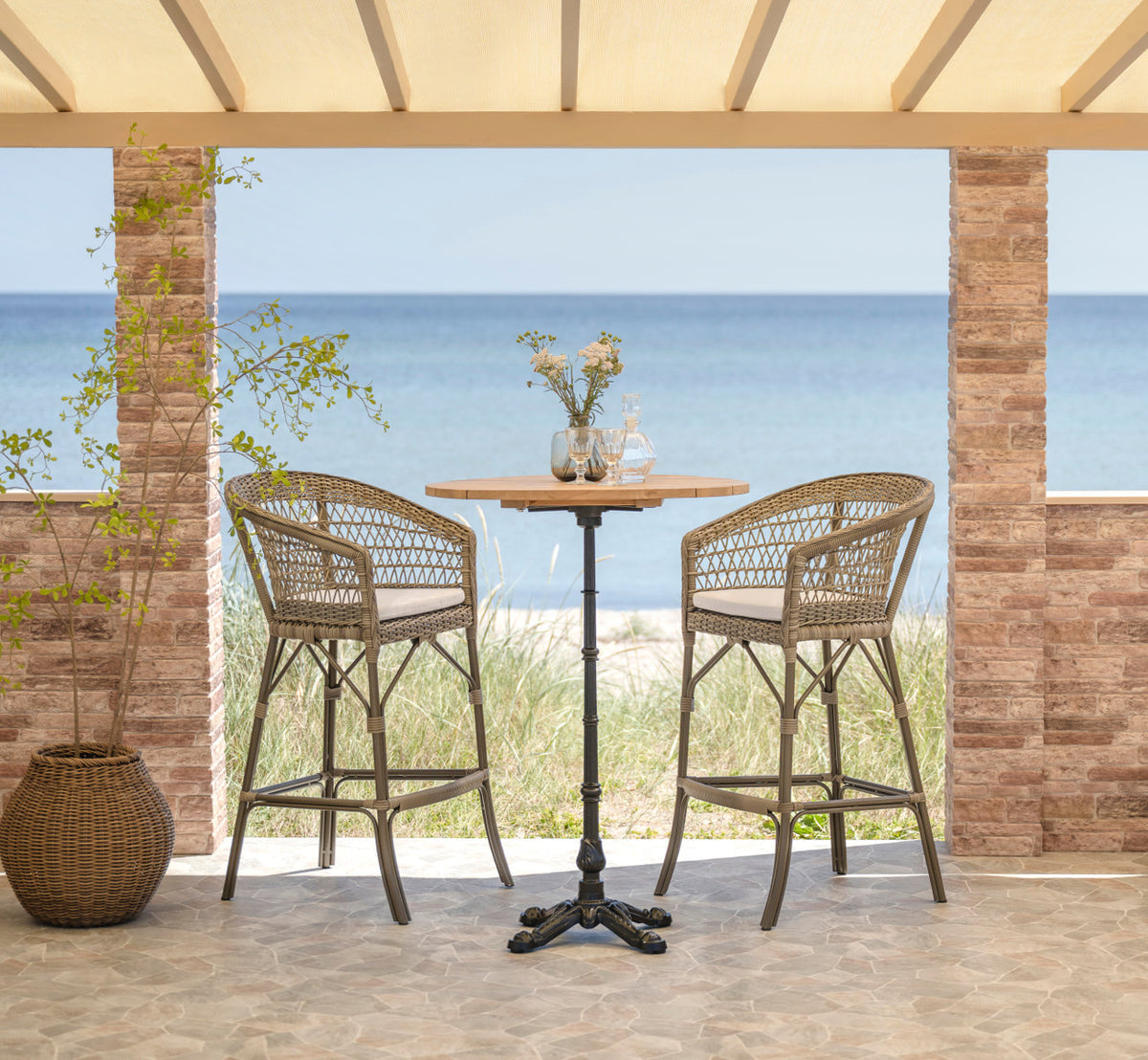Esta es una imagen de estilo de vida de Emma taburete de bar exterior en antique grey artfibre aluminium. Conjunto de bar con vista al mar.