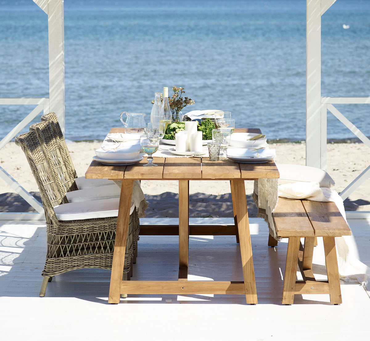 Esta es una imagen de estilo de vida de Marie Exterior Side Chair i antique grey artfibre aluminium. Junto a una mesa de teca en un pabellón junto al mar.