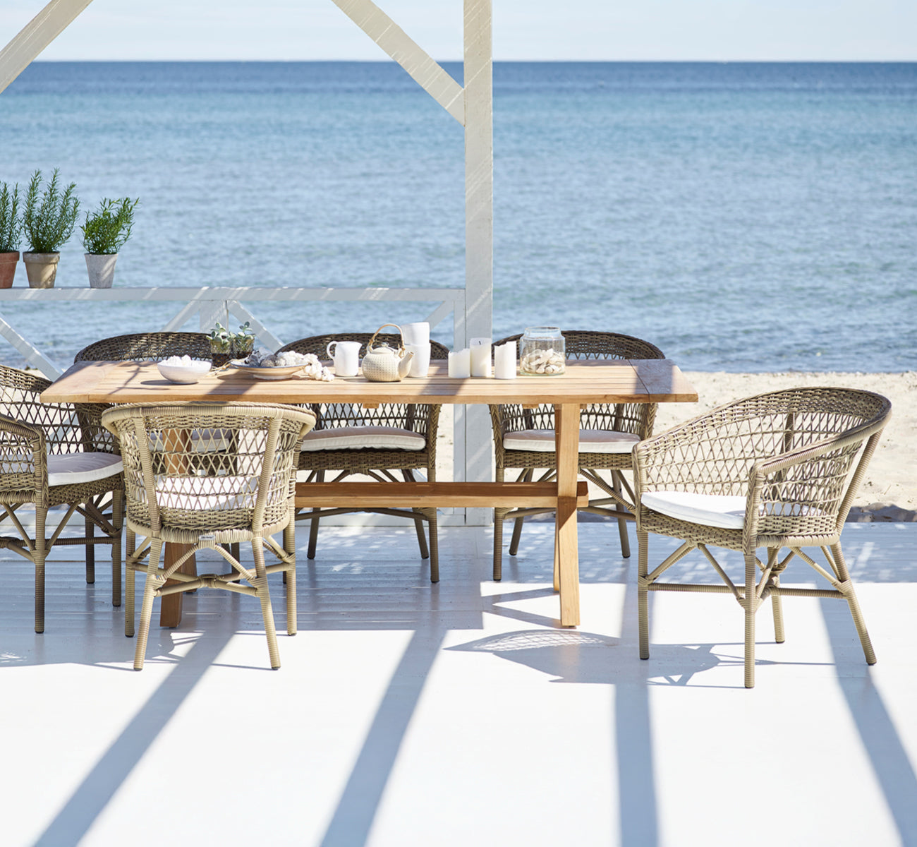 Esta es una imagen de estilo de vida de Emma silla de comedor exterior en antique Grey ArtFibre Aluminium, en una terraza costera luminosa con techo.
