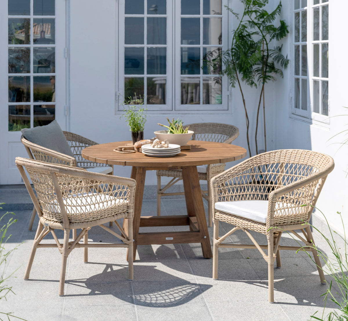 Esta es una imagen de estilo de vida de Emma silla de comedor exterior en natural ArtFibre Aluminium, en una terraza costera luminosa con techo de.
