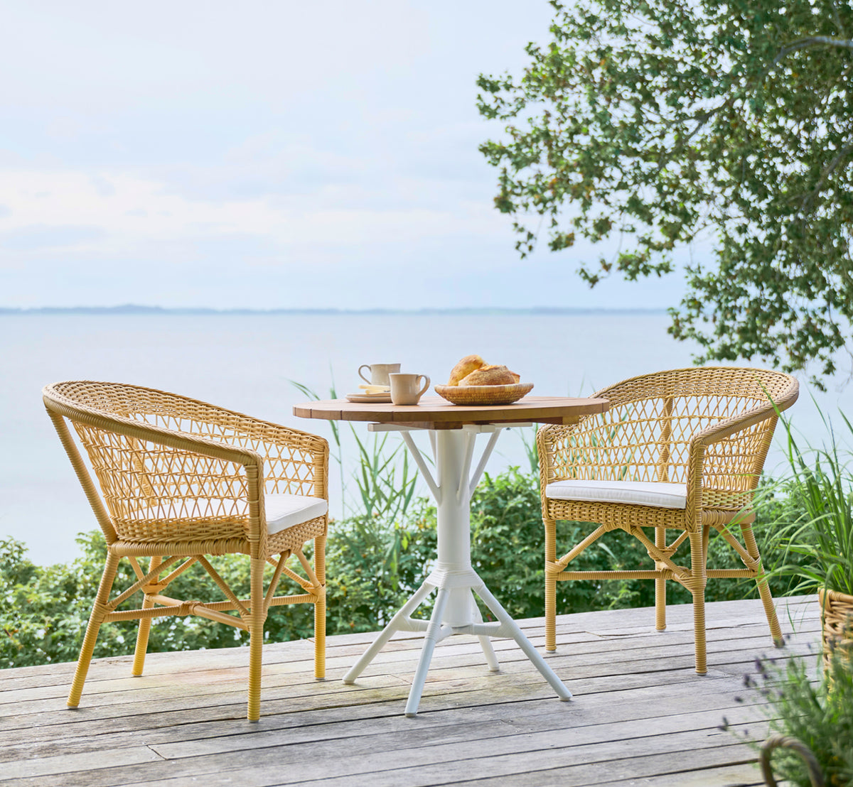 Esta es una imagen de estilo de vida de Emma silla de comedor exterior en natural ArtFibre Aluminium, en una terraza costera luminosa con techo de.