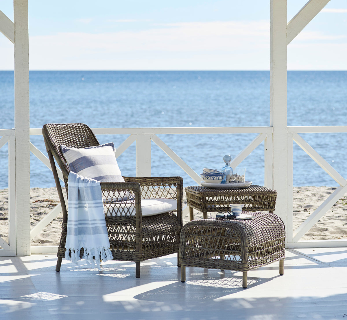 Esta es una imagen de estilo de vida de Dawn sillón lounge en antique Grey ArtFibre Aluminium, en una terraza costera con vistas al mar, gramíneas de.
