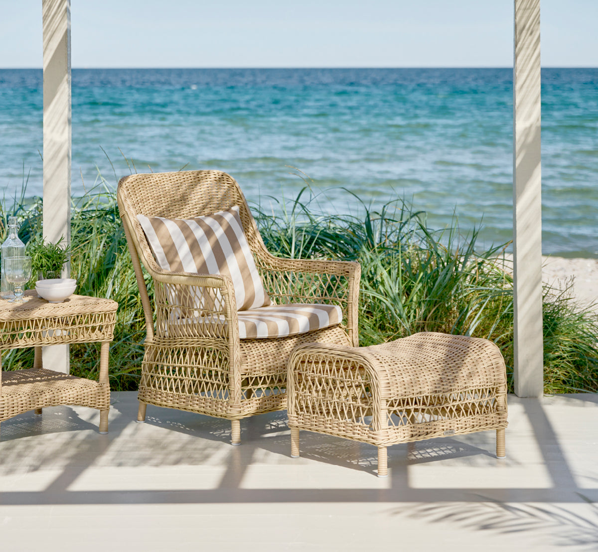 Esta es una imagen de estilo de vida de Dawn sillón lounge en natural ArtFibre Aluminium, en una terraza costera con vistas al mar, gramíneas de.