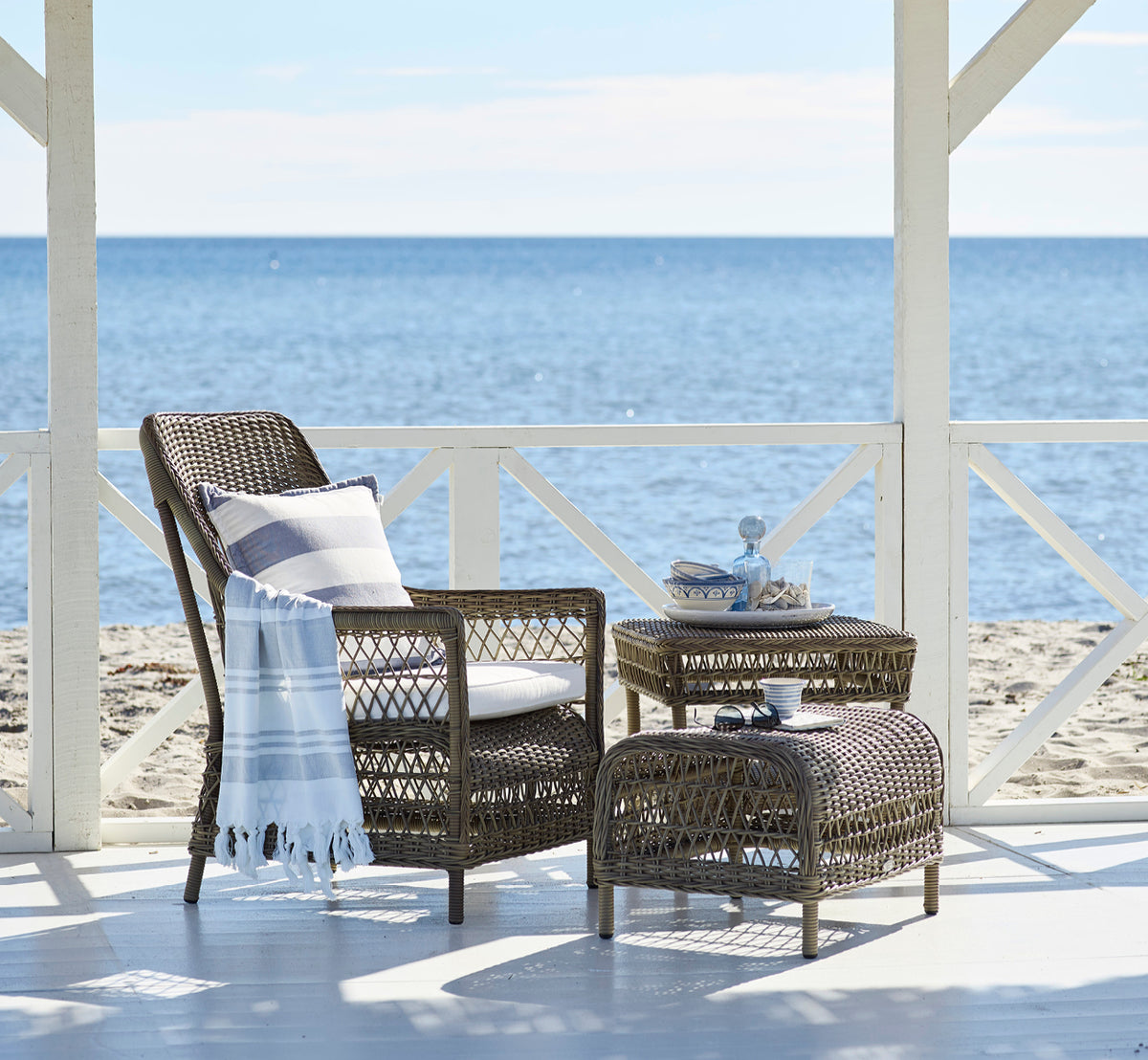 Esta es una imagen de estilo de vida de Dawn reposapiés en antique Grey ArtFibre Aluminium, en una terraza costera con vistas al mar, gramíneas de.