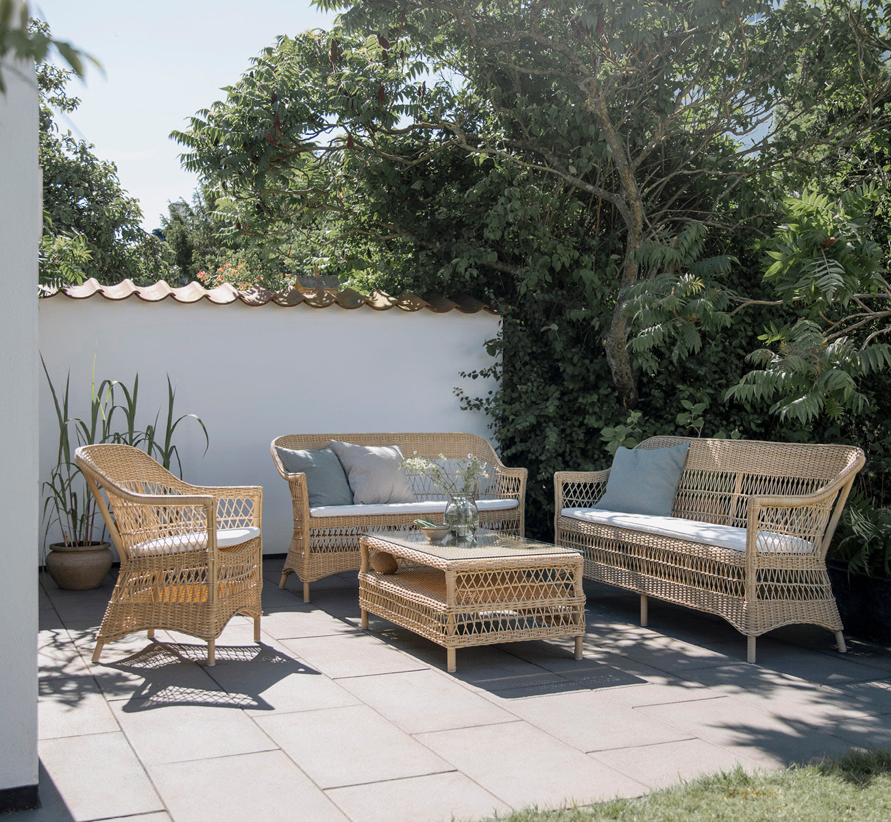 Esta es una imagen de estilo de vida de Charlot sofá de 2 plazas en natural ArtFibre Aluminium, en una terraza costera con techo de caña, vistas al.