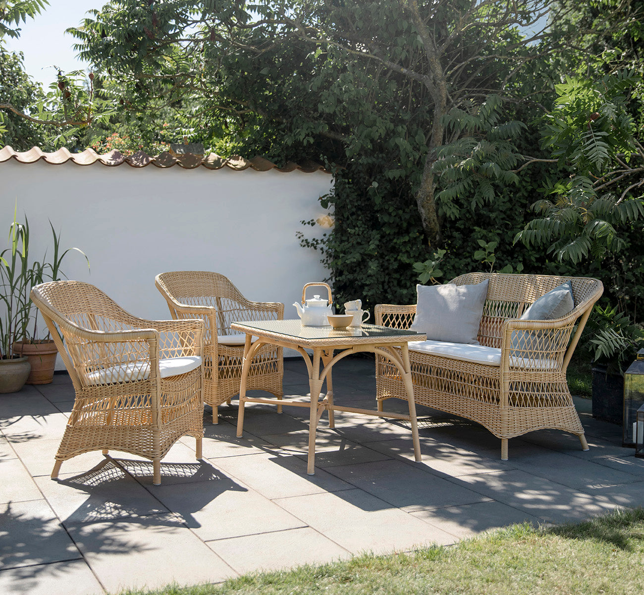 Esta es una imagen de estilo de vida de Charlot sofá de 2 plazas en natural ArtFibre Aluminium, en una terraza costera con techo de caña, vistas al.