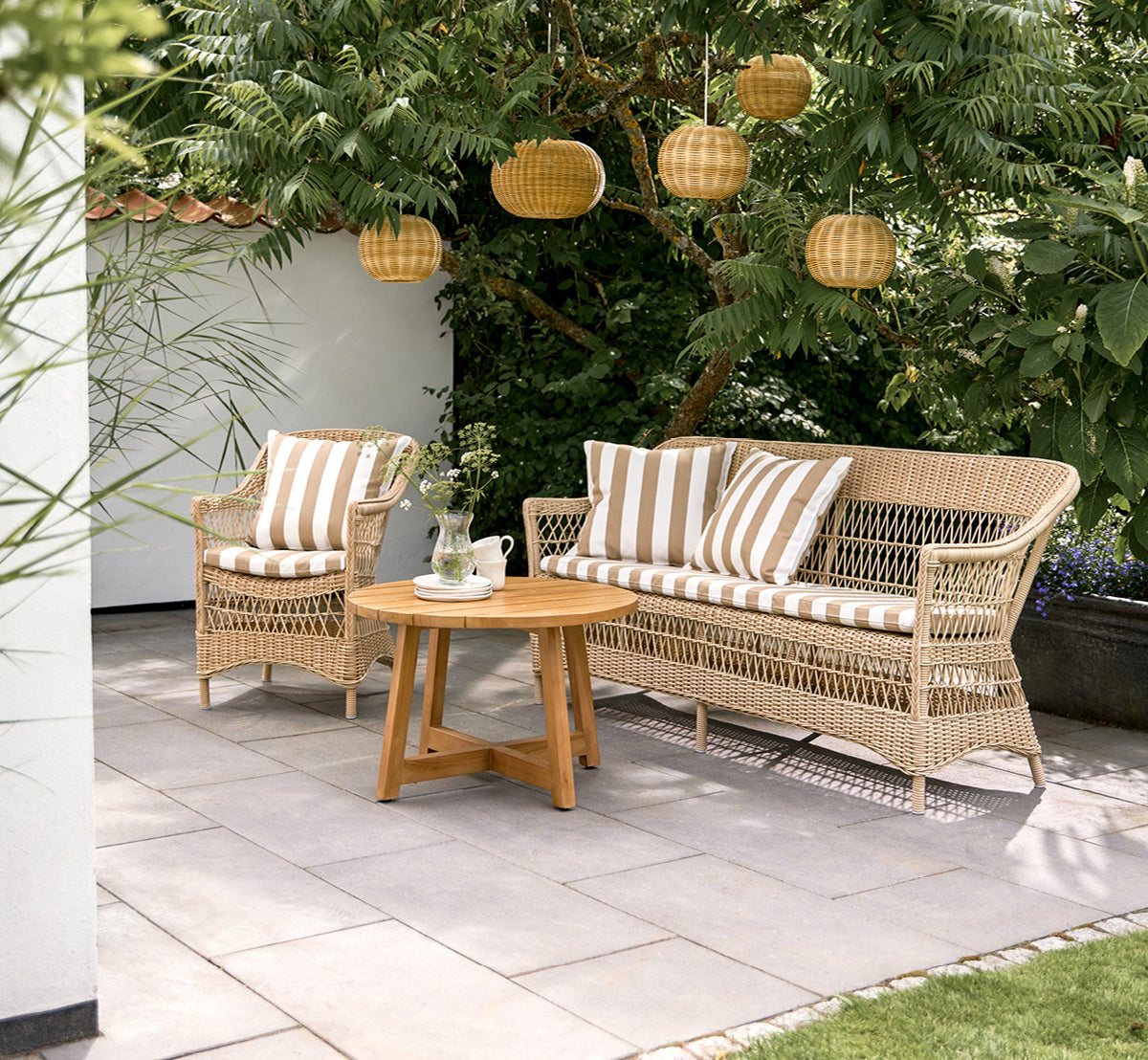 Esta es una imagen de estilo de vida de Charlot sofá de 3 plazas en natural ArtFibre Aluminium, en una terraza costera con techo de caña y vistas al.