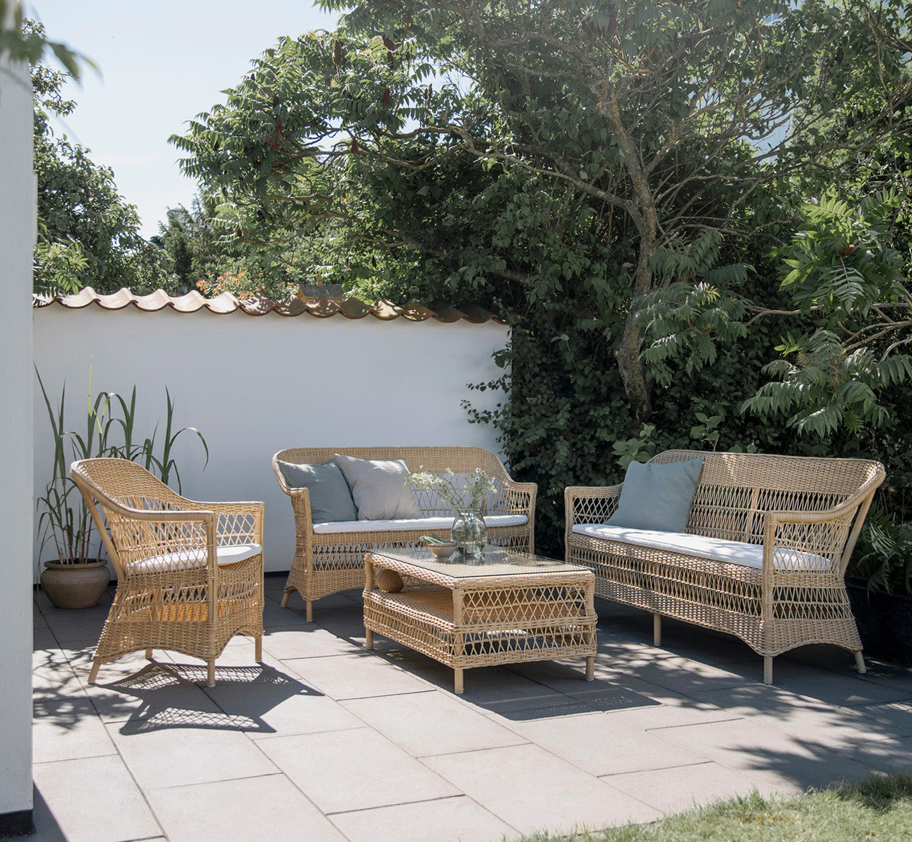 Esta es una imagen de estilo de vida de Charlot sofá de 3 plazas en natural ArtFibre Aluminium, en una terraza costera con techo de caña y vistas al.