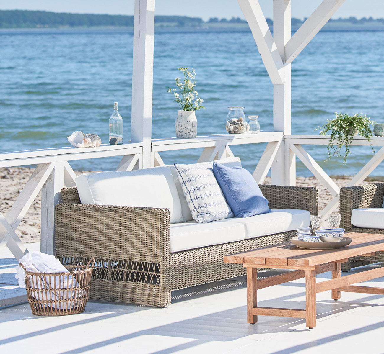 Esta es una imagen de estilo de vida de Carrie sofá en antique Grey ArtFibre Aluminium, en una terraza costera con cubierta de madera blanca, vistas.