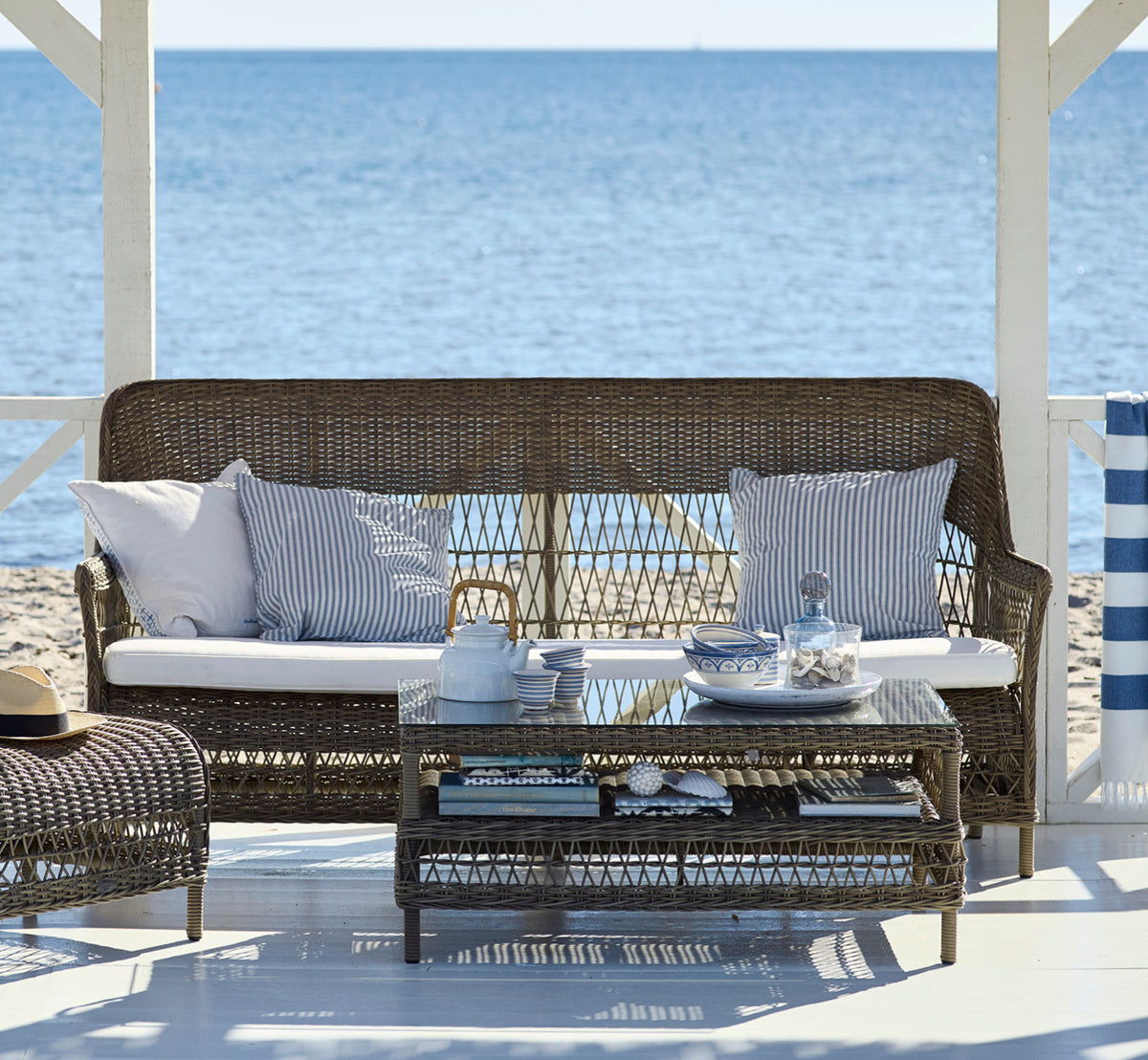 Esta es una imagen de estilo de vida de Dawn sofá en antique Grey ArtFibre Aluminium, en una terraza costera con cubierta de madera blanca y vistas.