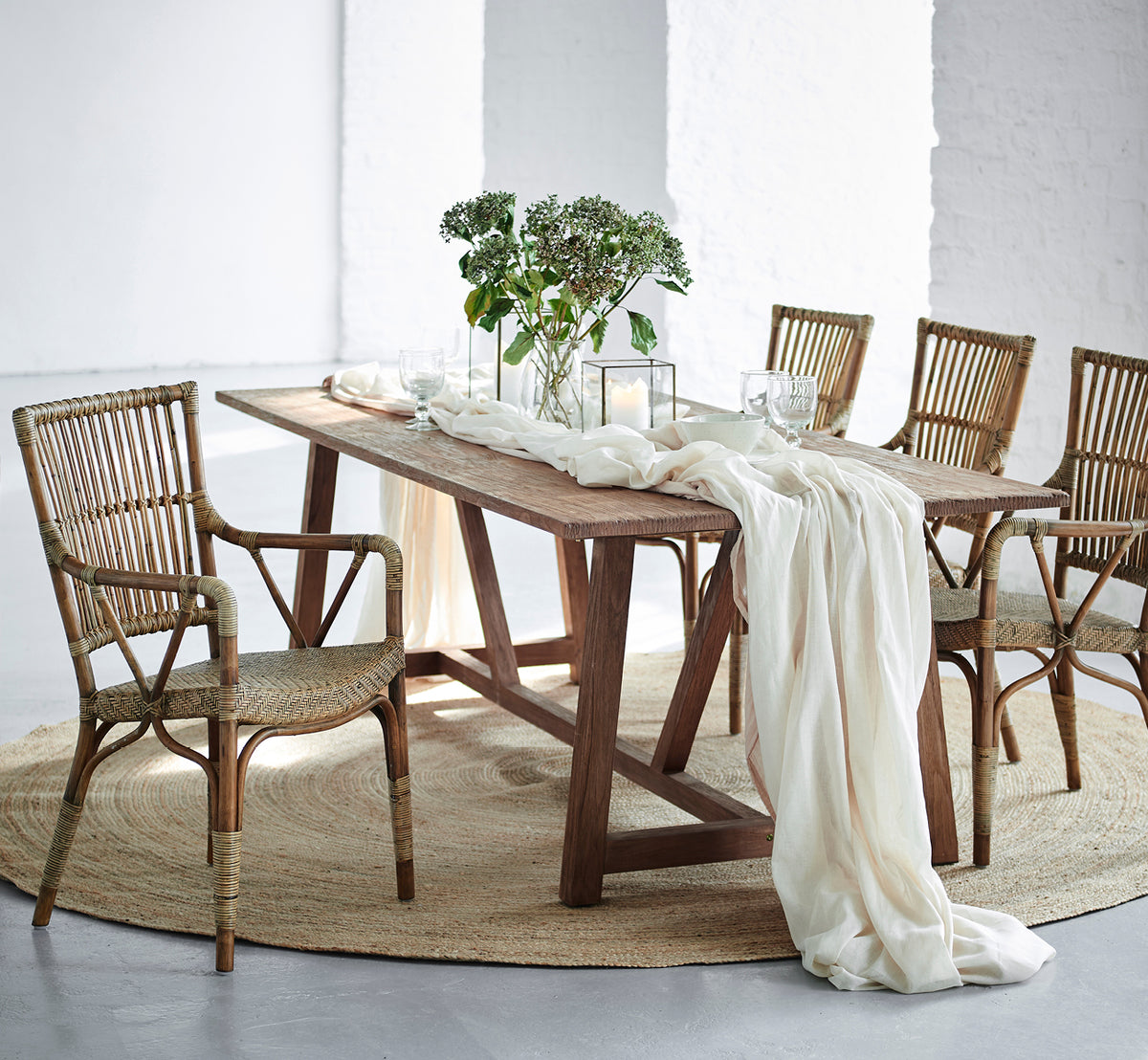 Esta es una imagen de estilo de vida de Lucas Teak Dining Table 240X100 cm en teak indoor. Cubierta con lino y vegetación, rodeada de sillas de ratán.