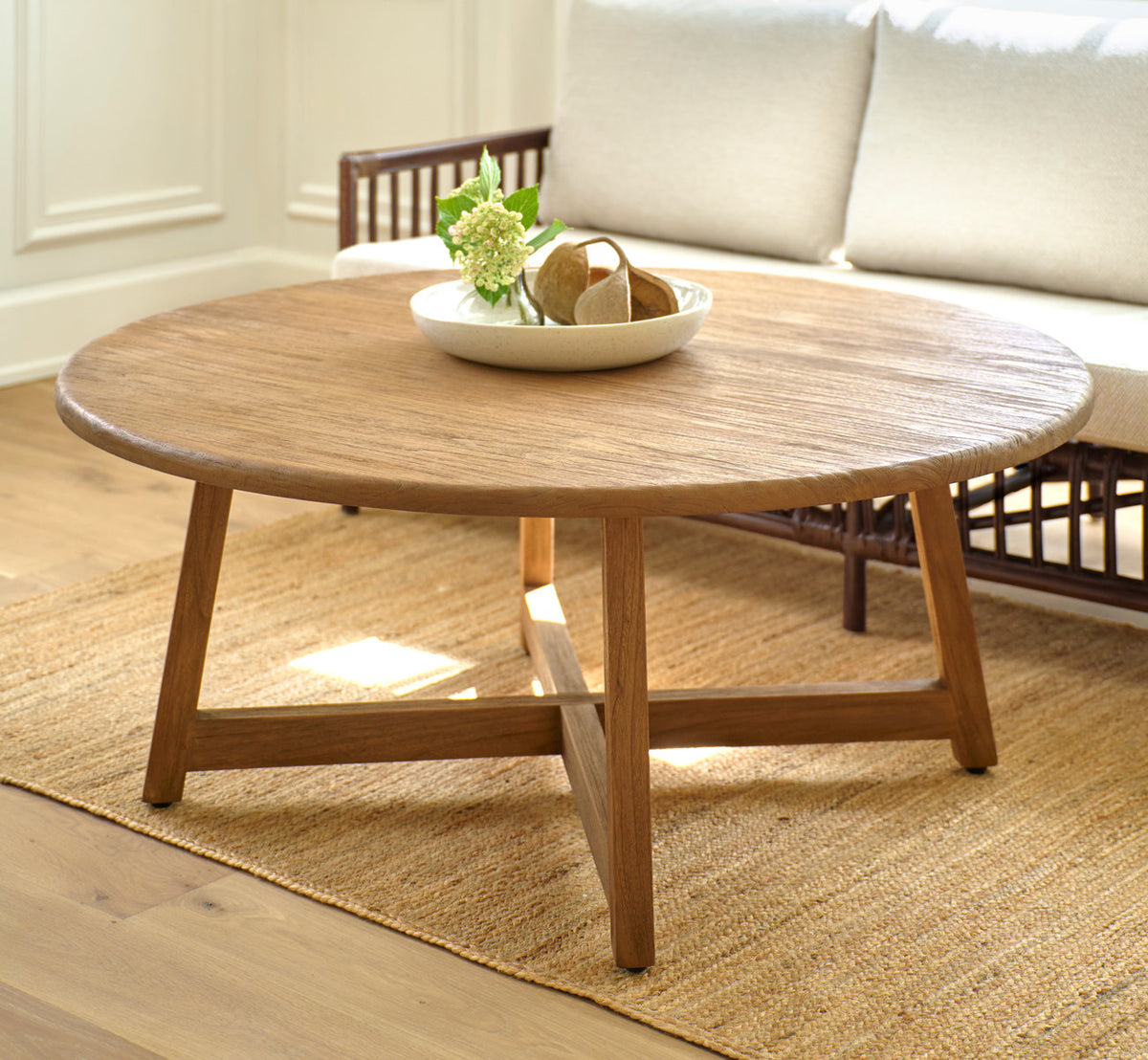 Esta es una imagen de estilo de vida de Aksel mesa de centro Ø120 cm en teak indoor. Con un cuenco de flores delante de un sofá de ratán.